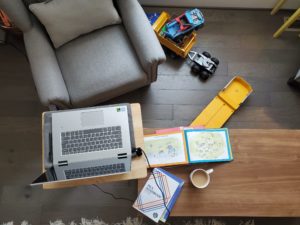 An overhead shot of an armchair, an open laptop, an MLA handbook, a cup of coffee, and children's toys