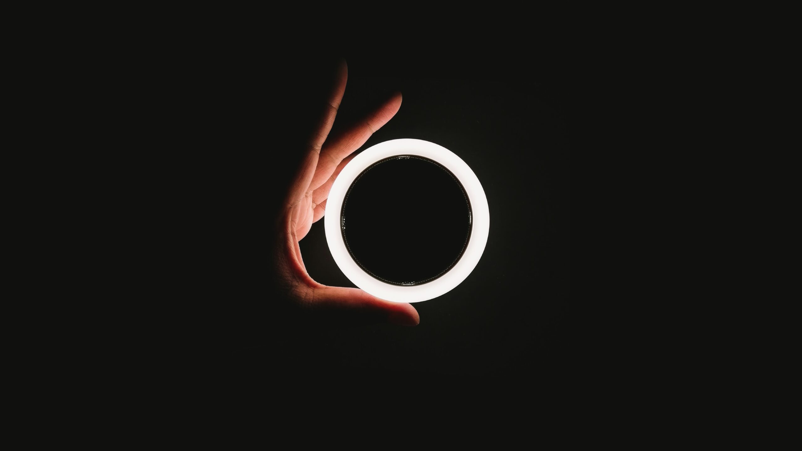 Black background with white hand holding a glowing ring light